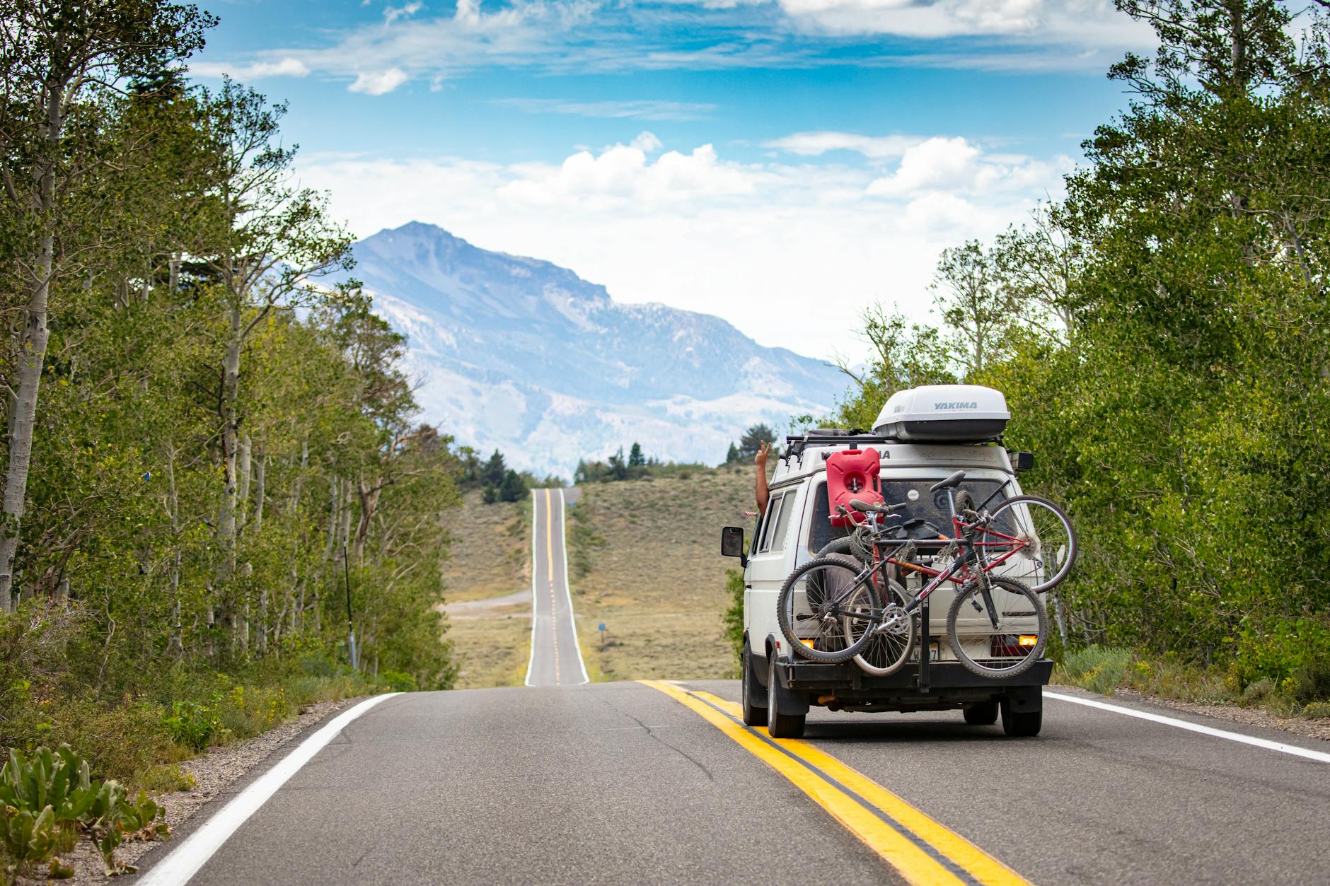 A camper van travels through a mountain landscape with bicycles mounted on the back