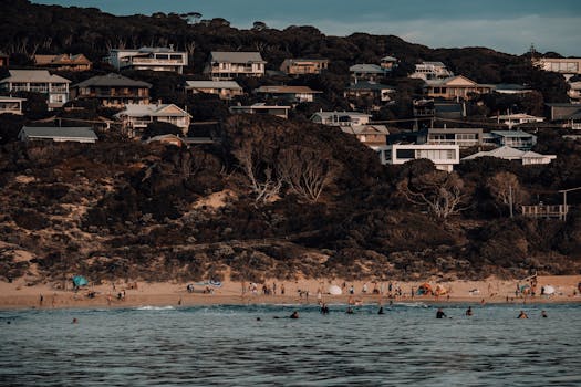 A beautiful beach scene with beachgoers and coastal houses under a clear summer sky.