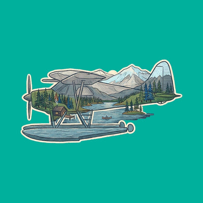 A float plane moored on a mountain lake with pine forest and snow capped peaks behind it, printed on a jade green cotton tee