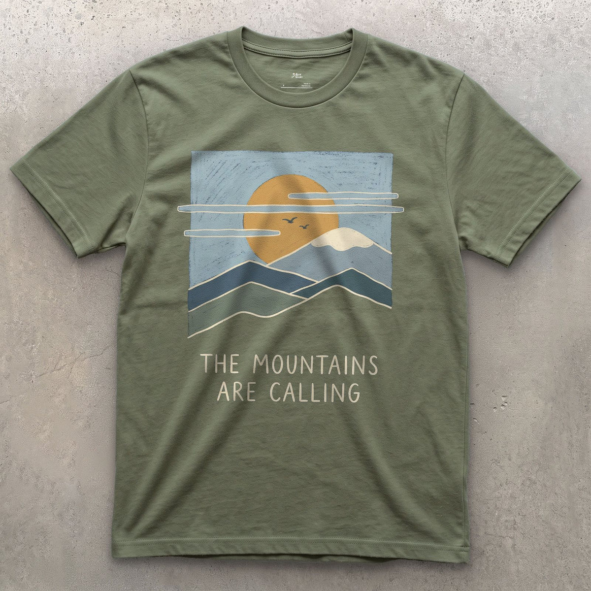 The Mountains Are Calling Over a Range at Sunset design on a Military Green Gildan Softstyle t-shirt